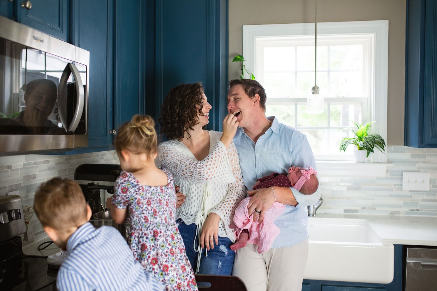 Laughing couple in casual clothing share playful moments together in a bright kitchen.