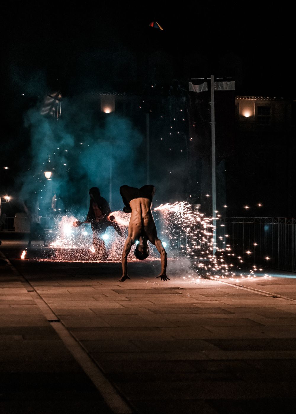Acrobatic performance with sparks and fire effects in a dark outdoor setting.
