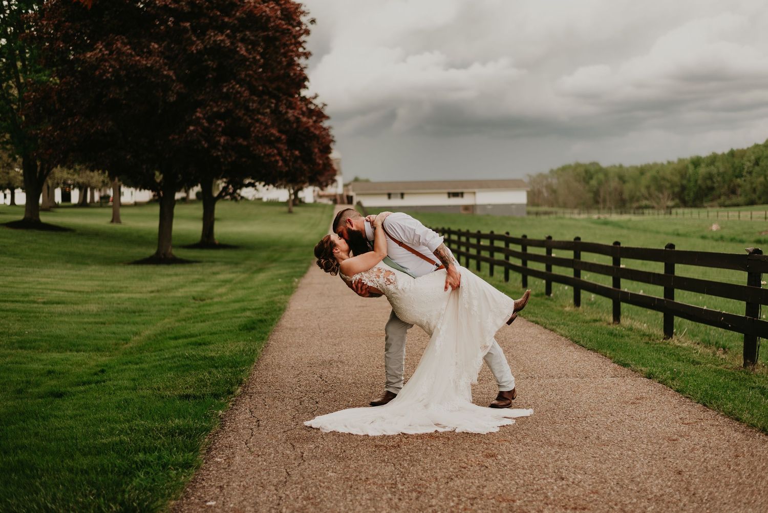A romantic dip pose of newlyweds on a tree-lined path with wooden fencing in Stark County, Ohio.