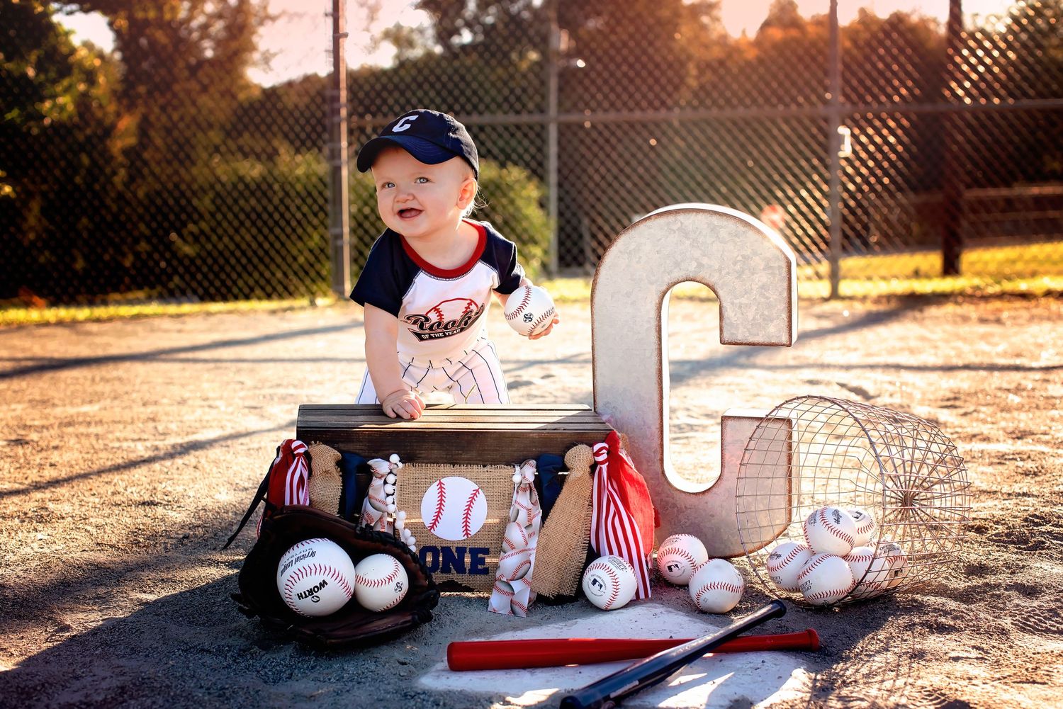 Baseball gear including gloves, baseballs, and a cap arranged on wooden planks at sunset.