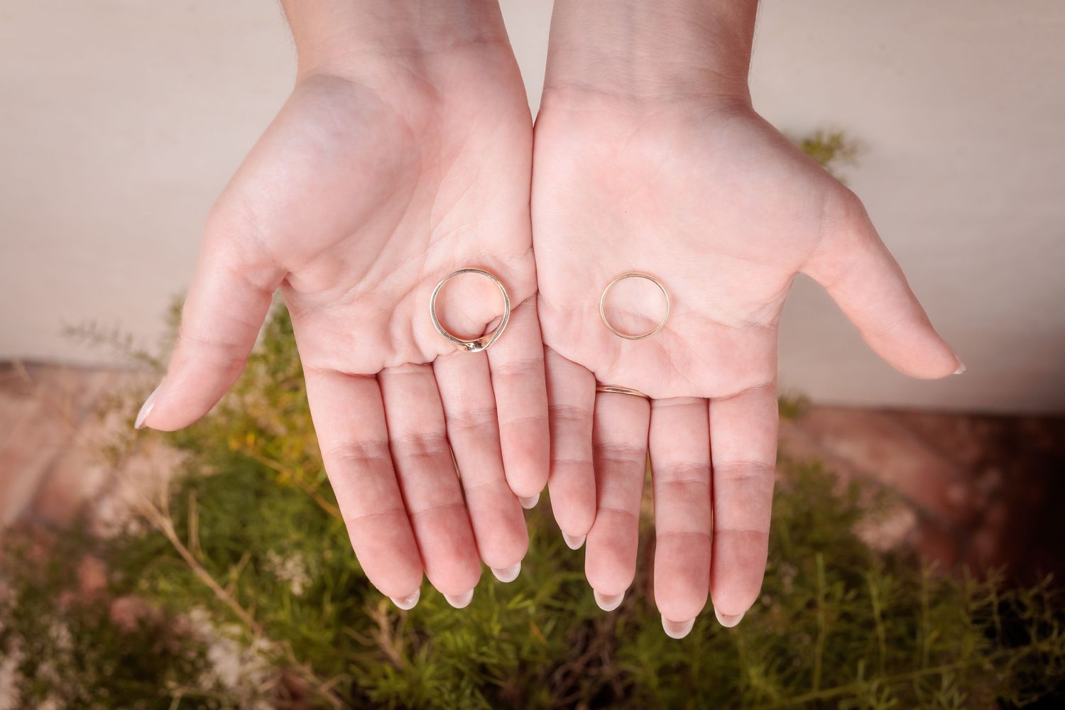 Close-up of hands displaying wedding rings against a natural mossy background.