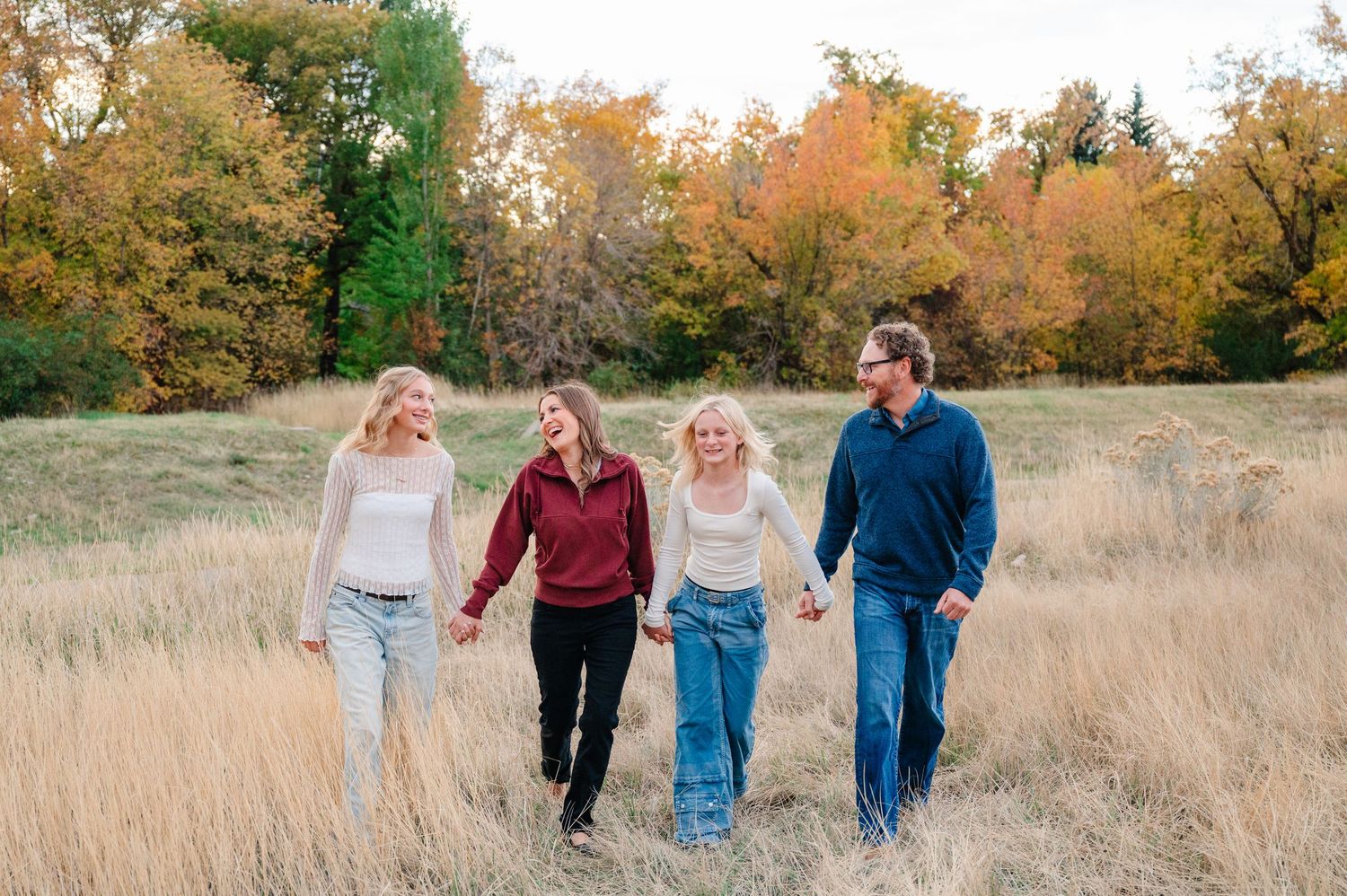 A family walks together through a golden autumn field during sunset while holding hands and smiling.