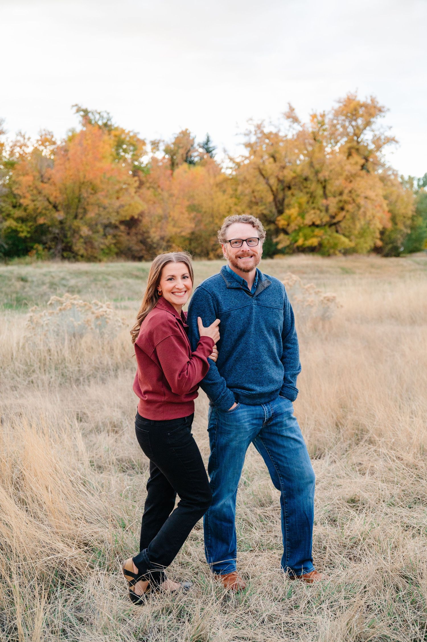 A couple shares playful moments together in a golden autumn field during an outdoor photo session.