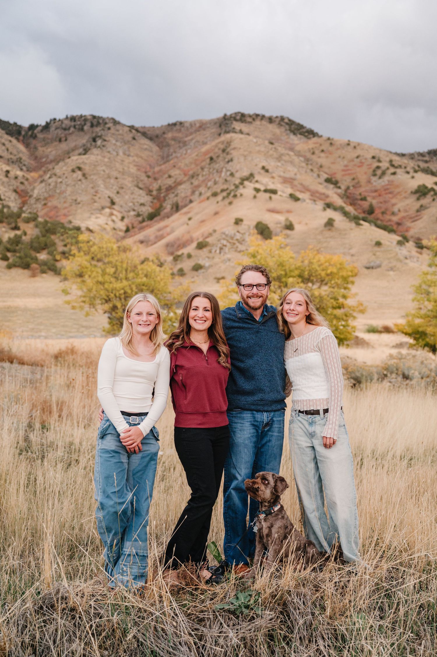 Group portrait in casual attire standing together in a grassy field with autumn mountains in the background.