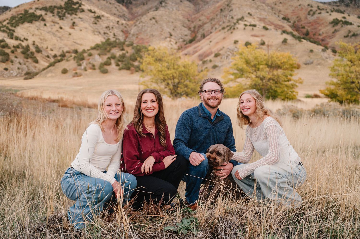 A group lounges together in golden autumn grass against a backdrop of desert hills during sunset.