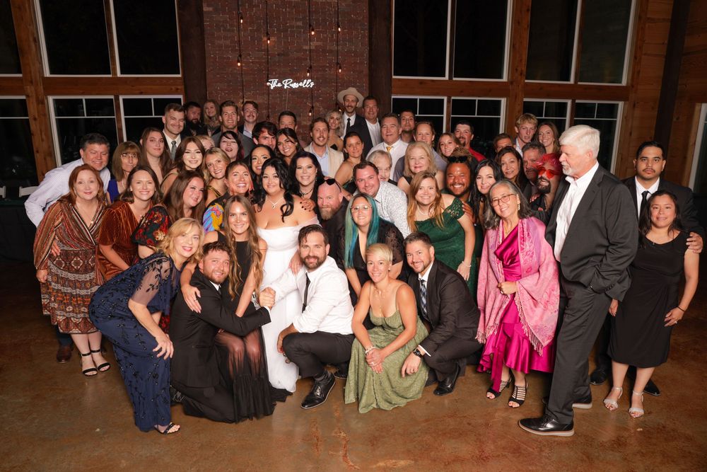 Large group of formal event attendees posing together in a panoramic photo against a brick wall background.