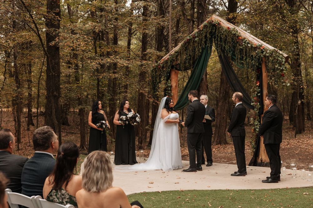Wedding ceremony in a serene forest setting with guests gathered on a stone path surrounded by tall trees.