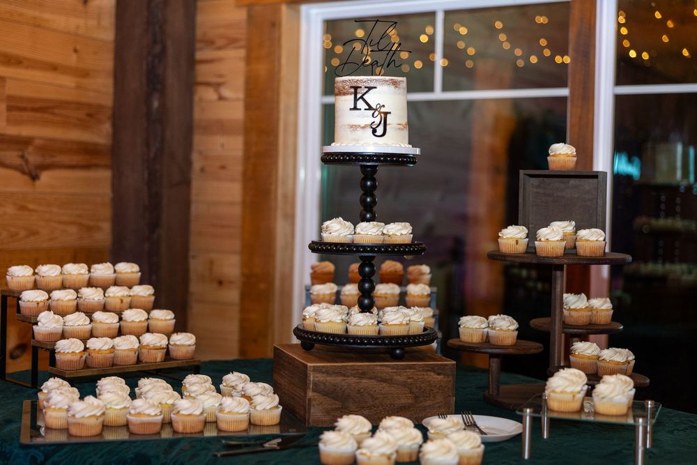 Rustic wooden wall display with tiered white cupcakes arranged on stands with twinkle lights in the background.