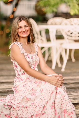 Floral dress portrait on wooden deck with garden furniture in background.