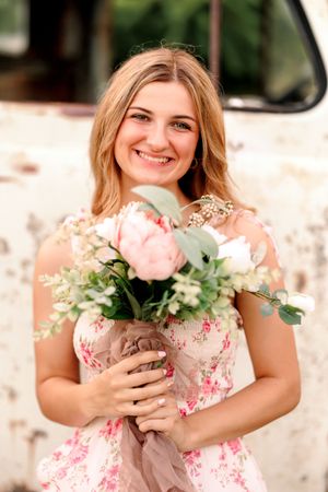 Portrait session in a garden setting with pink floral bouquet and soft natural lighting.