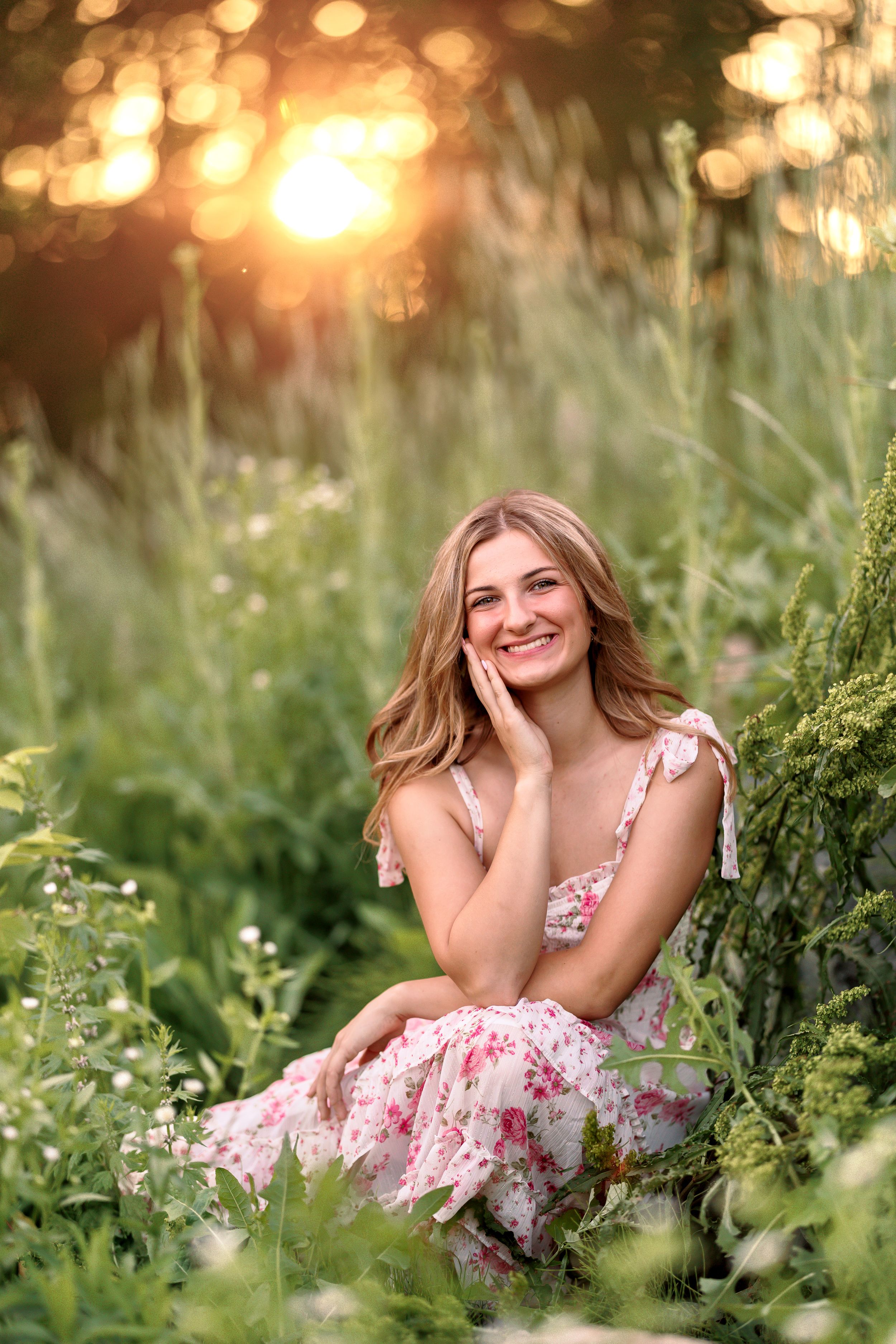 Dreamy outdoor portrait in floral dress amid tall grass at golden hour.