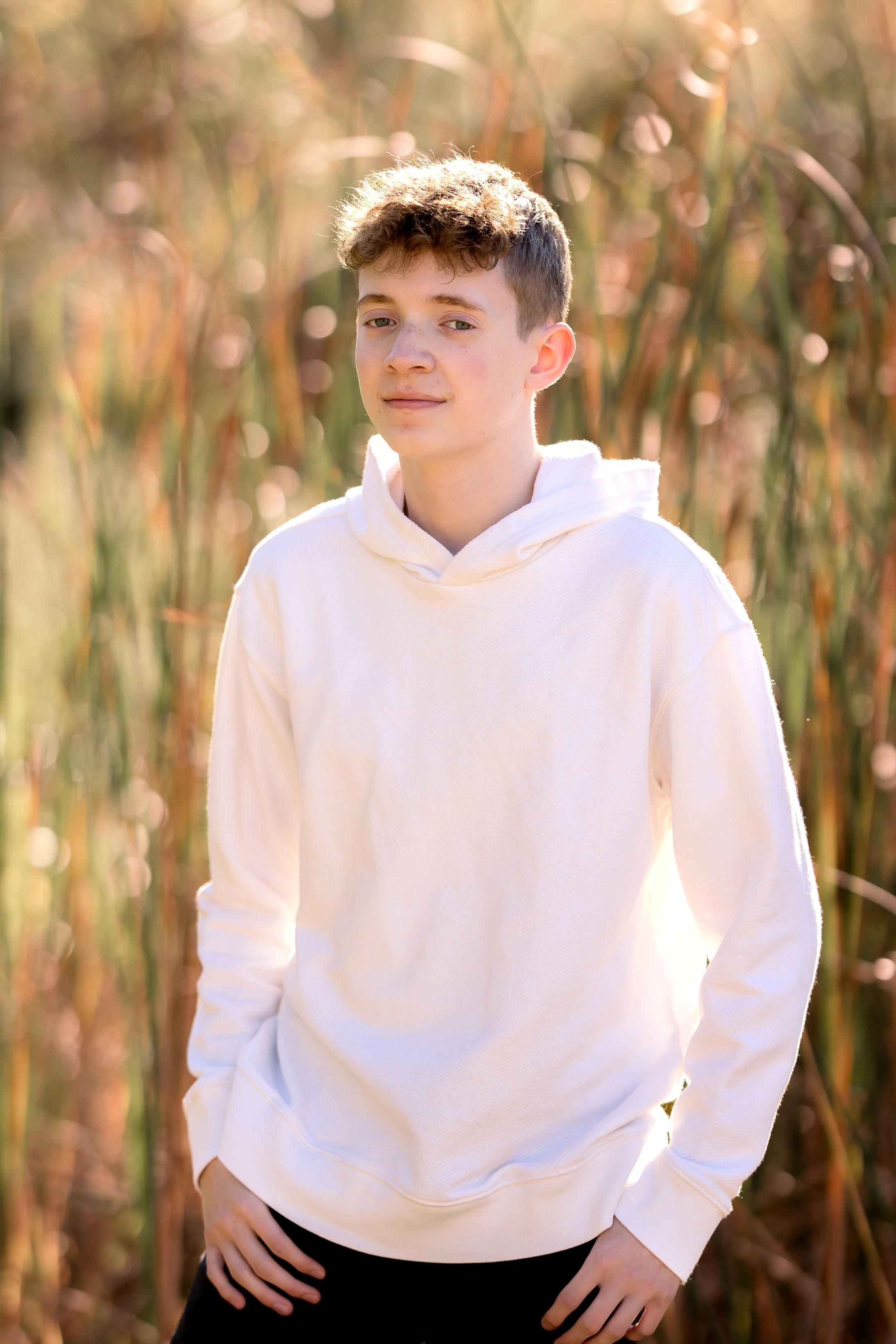 Casual outdoor photoshoot in tall grass with white hoodie against natural background.