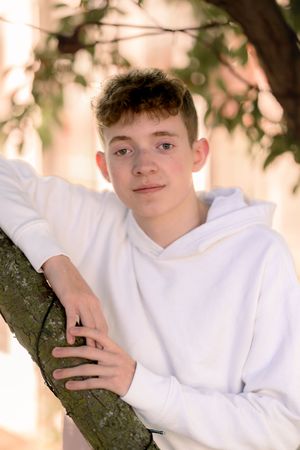 Relaxed poses leaning against tree trunk in natural outdoor setting.