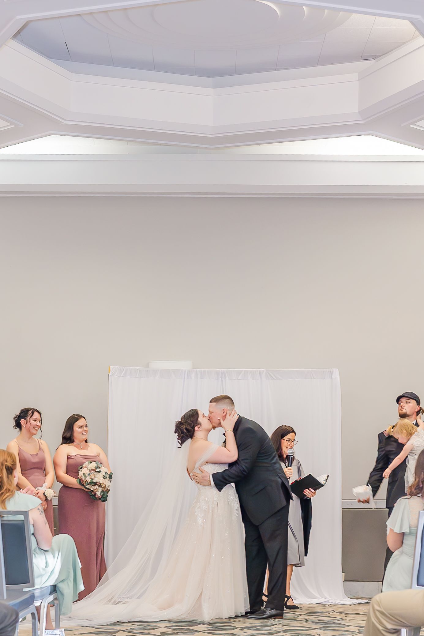 Wedding party poses for creative dip photos during reception in elegant white ballroom.