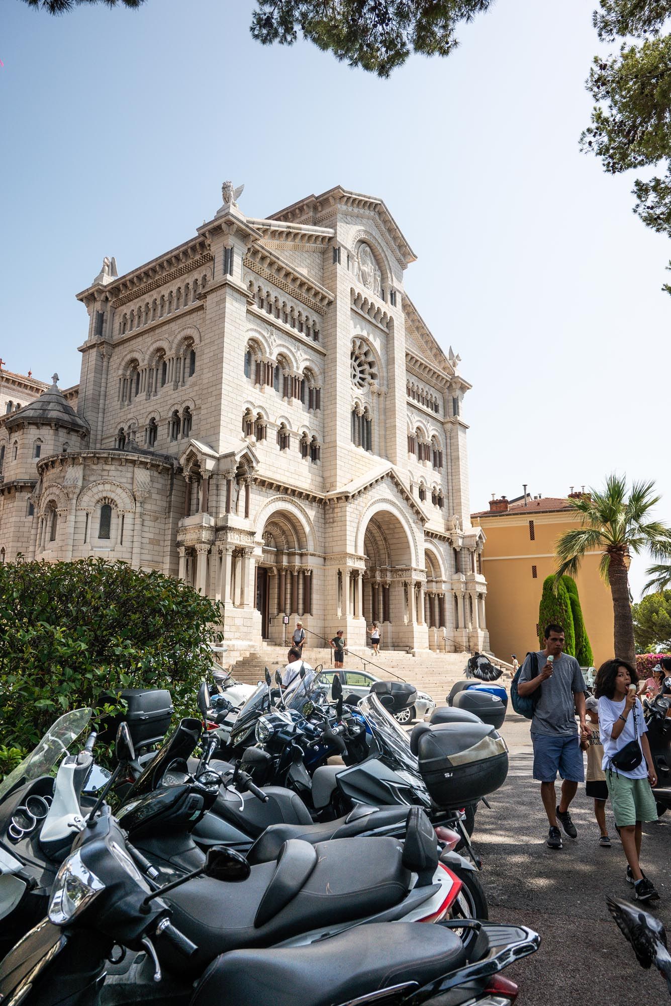 Motorcycles parked in front of the historic Monaco Cathedral, a Romanesque-Byzantine church with ornate architecture.