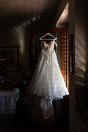 Wedding dress hanging in dramatic window light creating beautiful shadows and highlights.