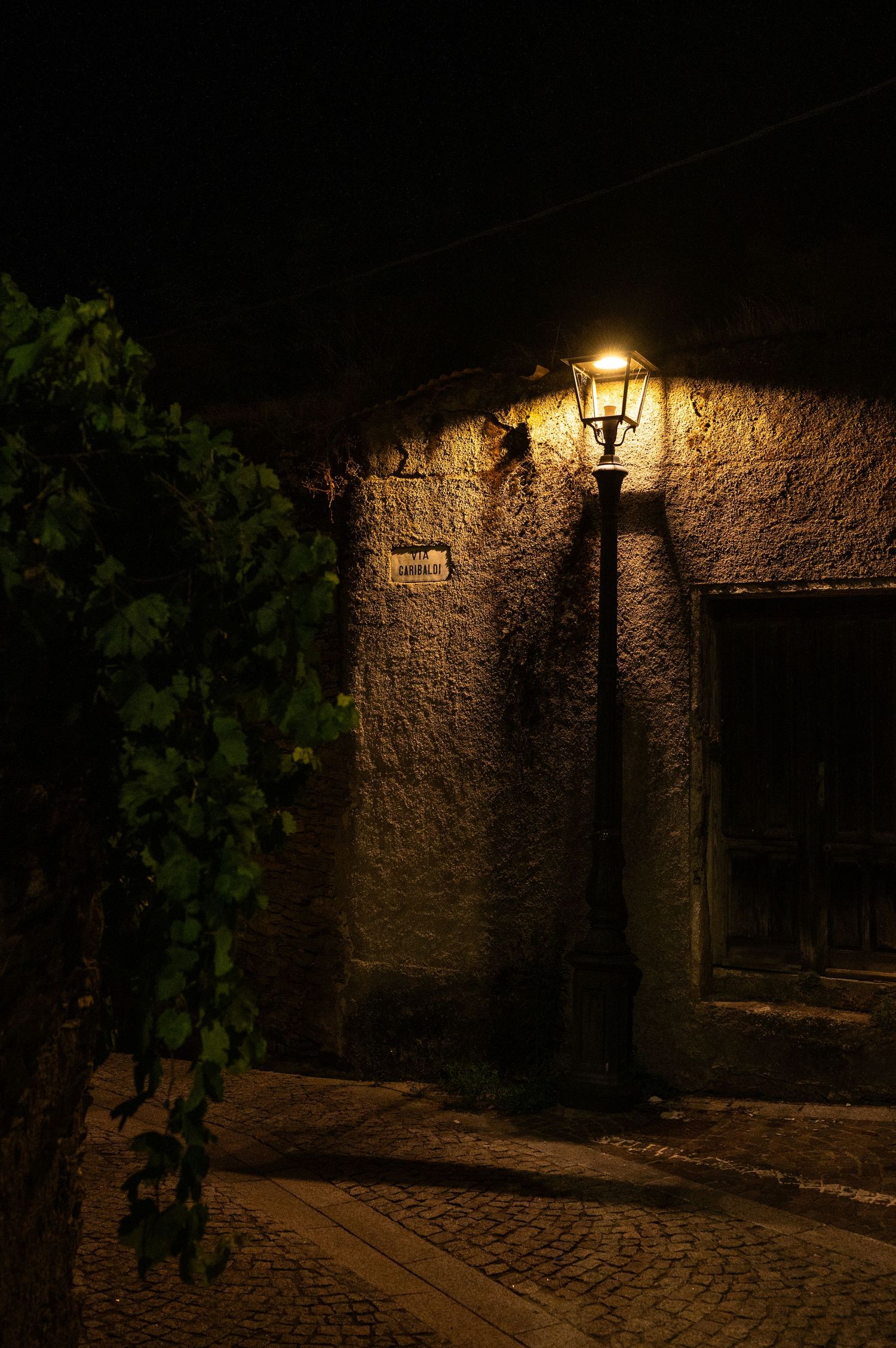 Vintage street lamp illuminating stone wall and cobblestone path at night.