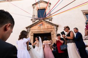 Wedding guests celebrating outside a rustic church building with red string decorations.