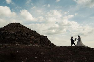 Silhouettes against a cloudy sky on a rocky mountain ridge during a wedding photoshoot.