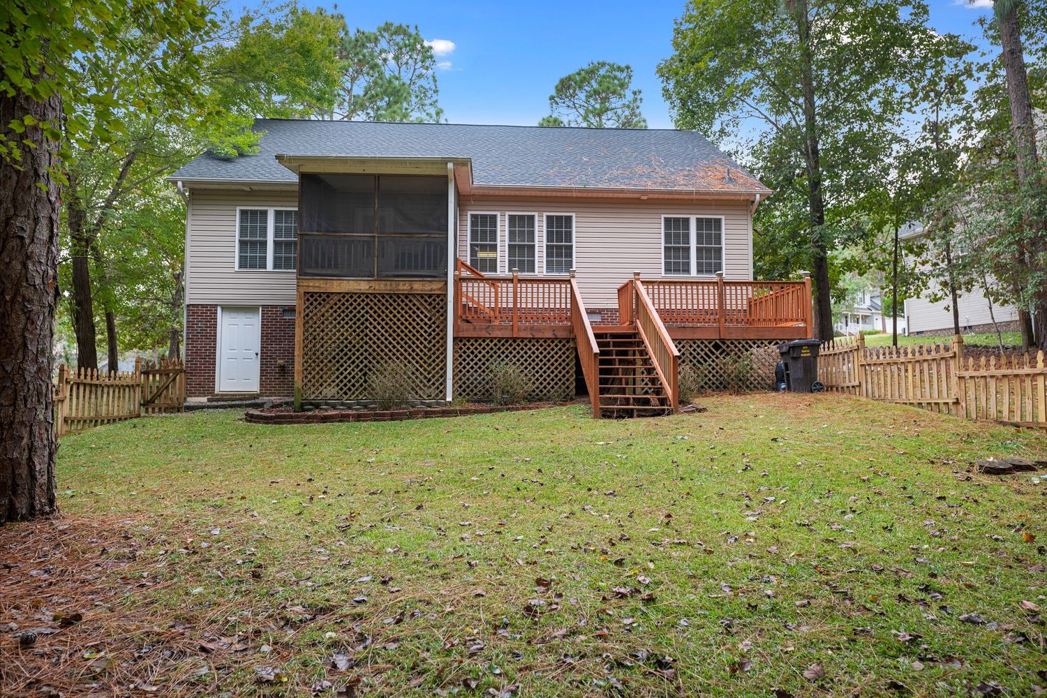 Panoramic view of a spacious backyard with green grass and mature trees surrounding a residential property.