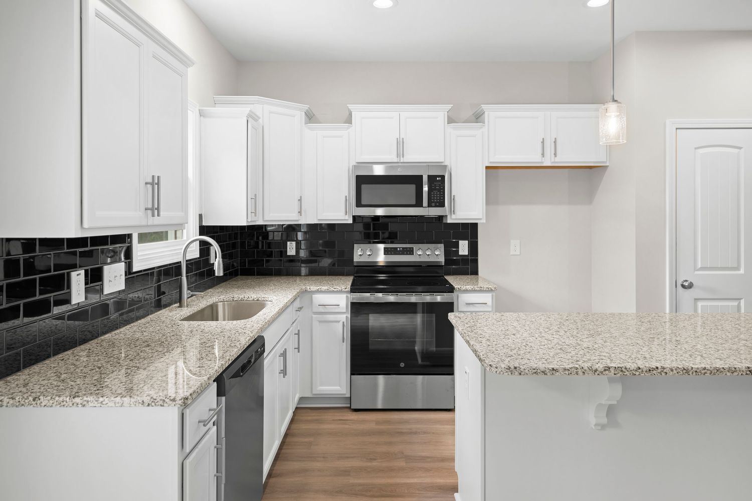 White kitchen with black subway tile backsplash, granite counters, and black appliances in a galley layout.