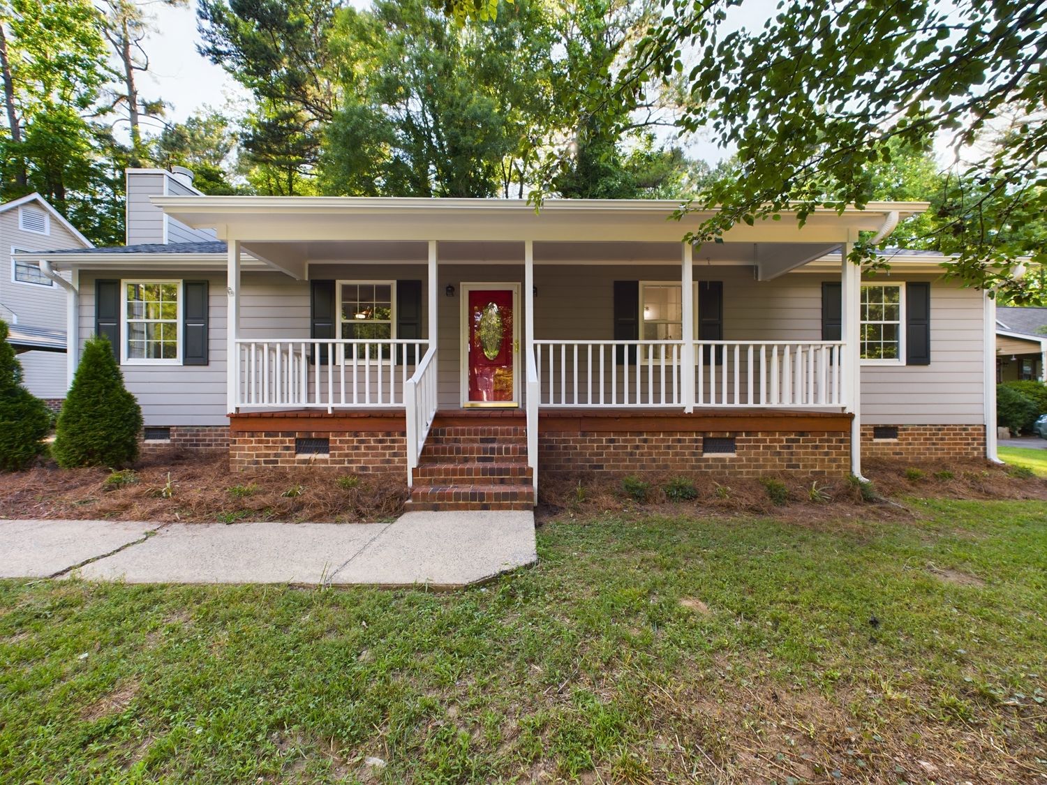 Charming ranch house with covered front porch, white siding, and brick foundation surrounded by landscaping.