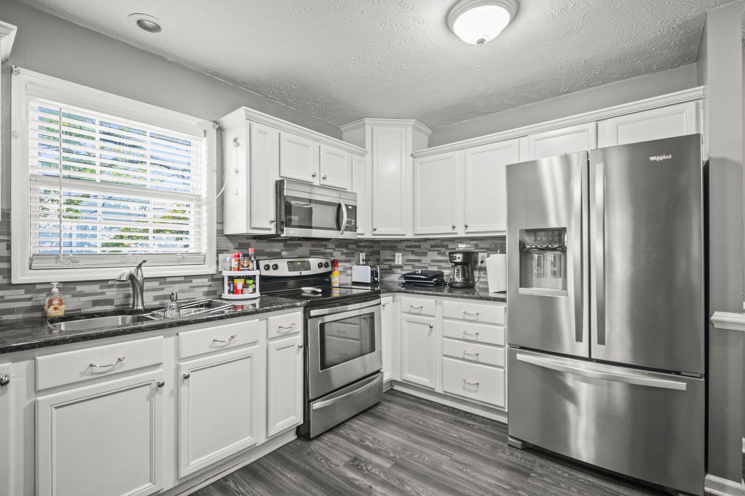 Modern white kitchen with stainless steel appliances and bright lighting.