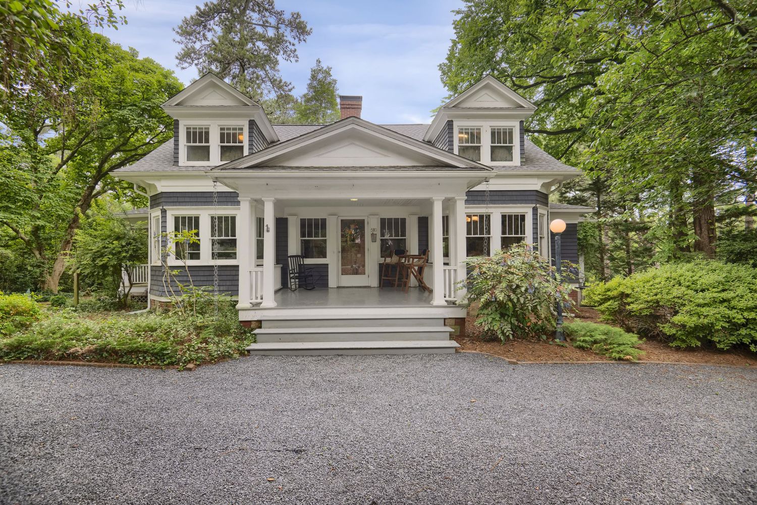 White colonial houses nestled among lush green trees with gravel driveways.