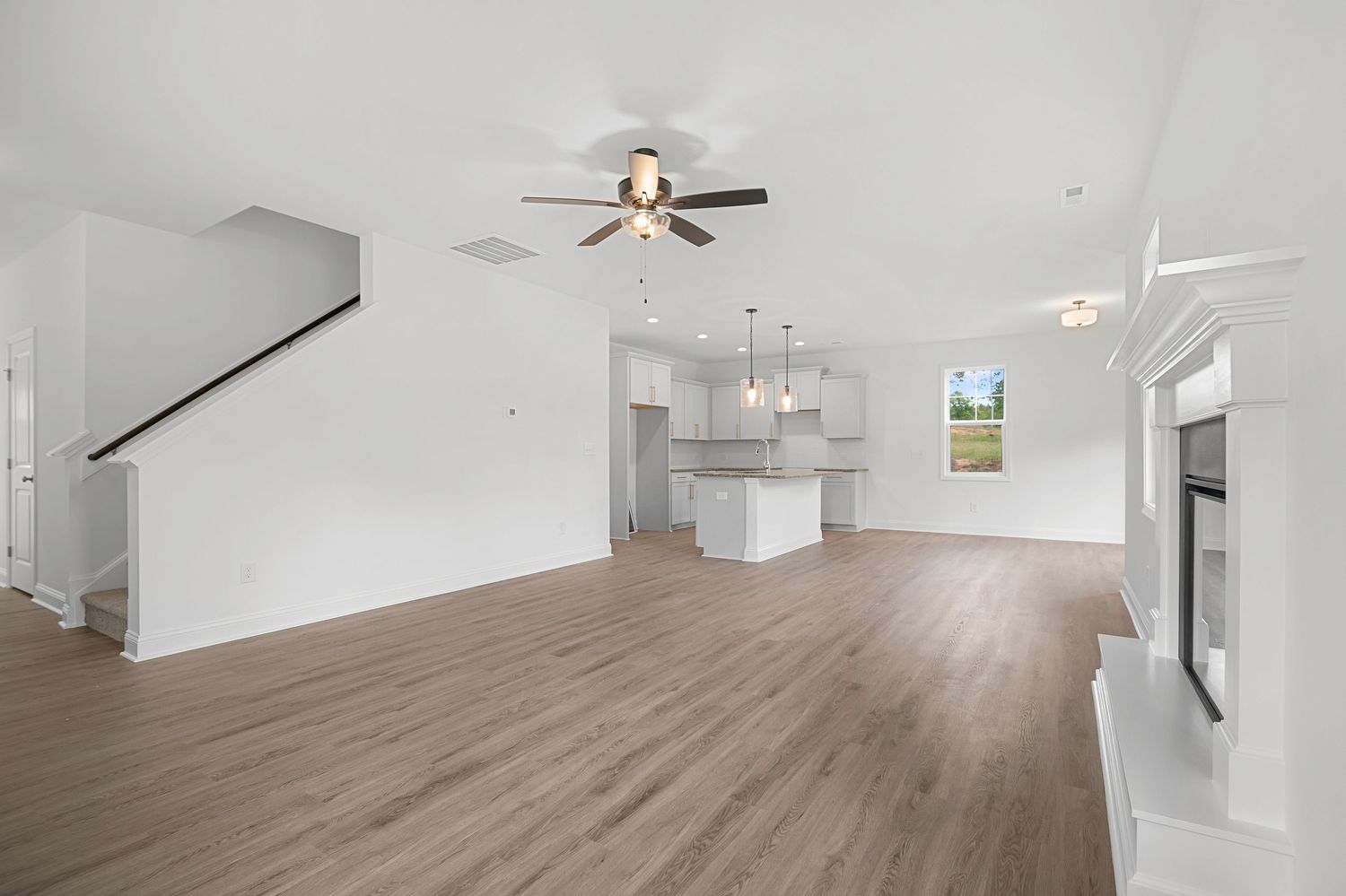 Spacious empty living room with ceiling fan and light wood flooring.