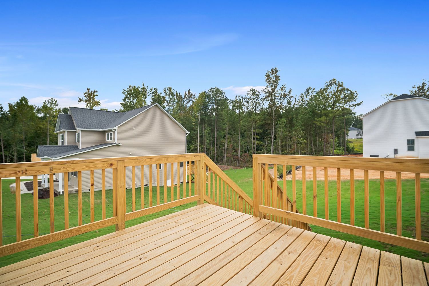 New wooden deck with railing overlooking a green lawn and residential homes in background.