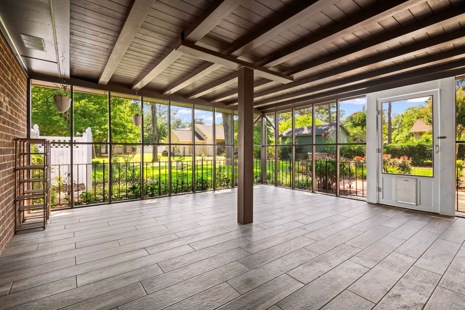 Covered outdoor patio with wooden beams and tile flooring overlooking a lush green backyard.