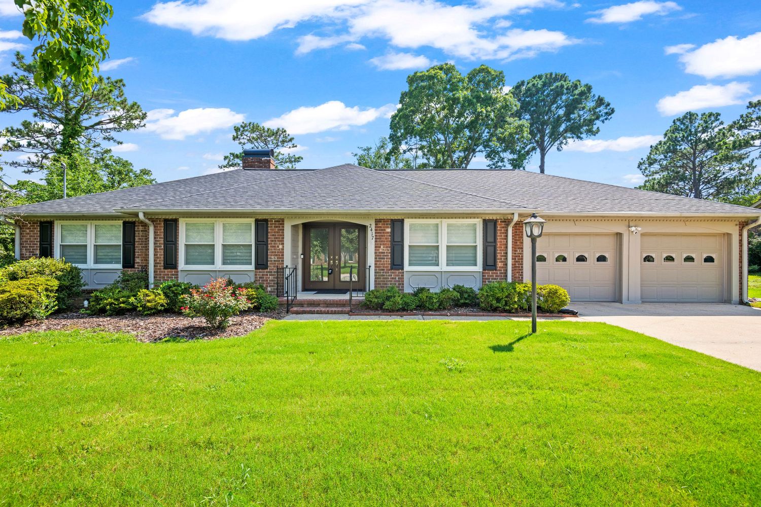 Ranch-style home with brick exterior, attached two-car garage, and manicured lawn under blue skies.