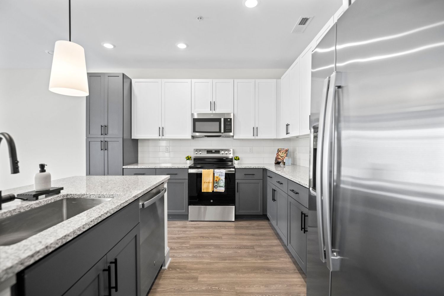 Modern kitchen with white upper cabinets, dark lower cabinets, and stainless steel appliances featuring granite countertops.