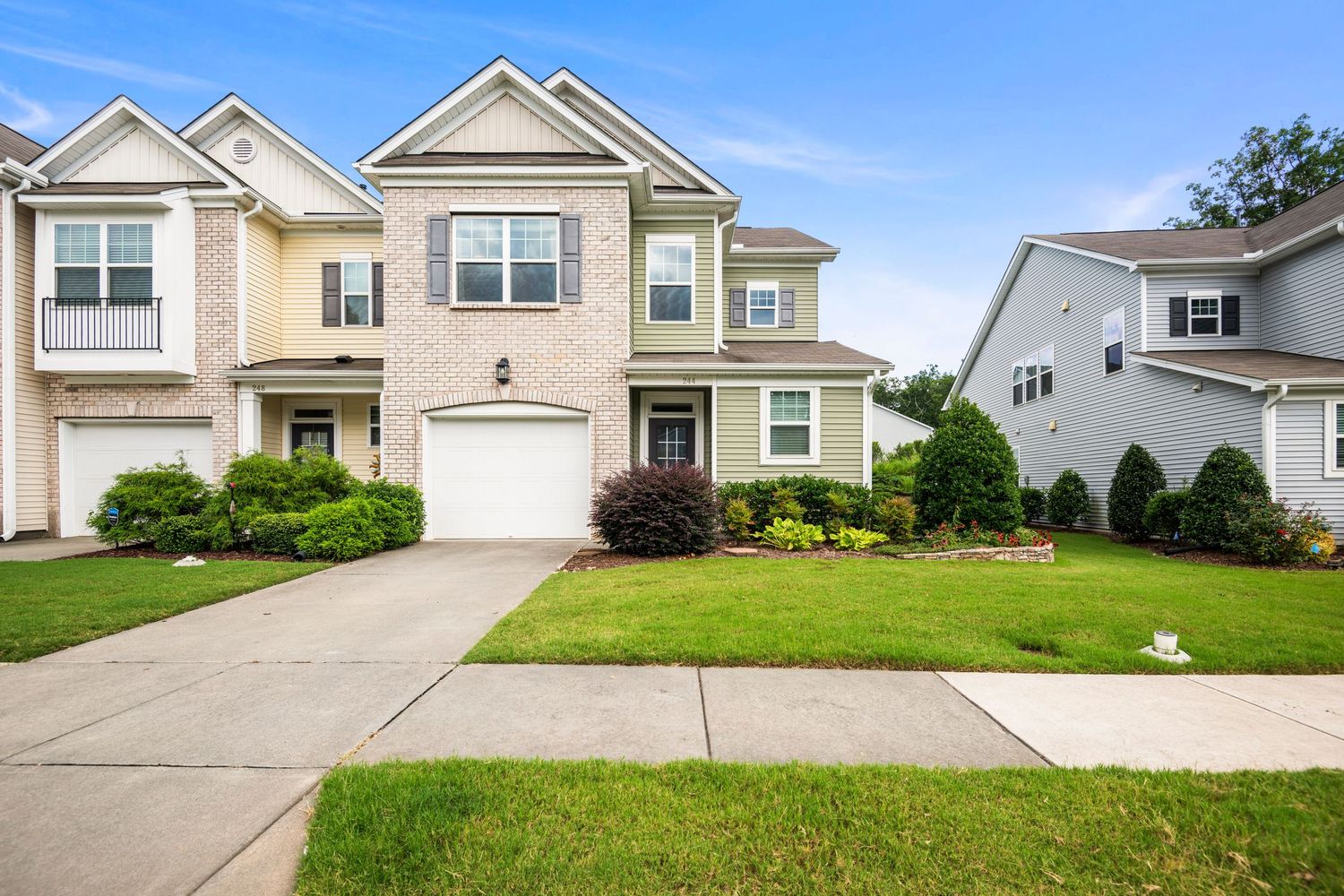 Row of suburban houses with white exterior and green lawns under blue sky.