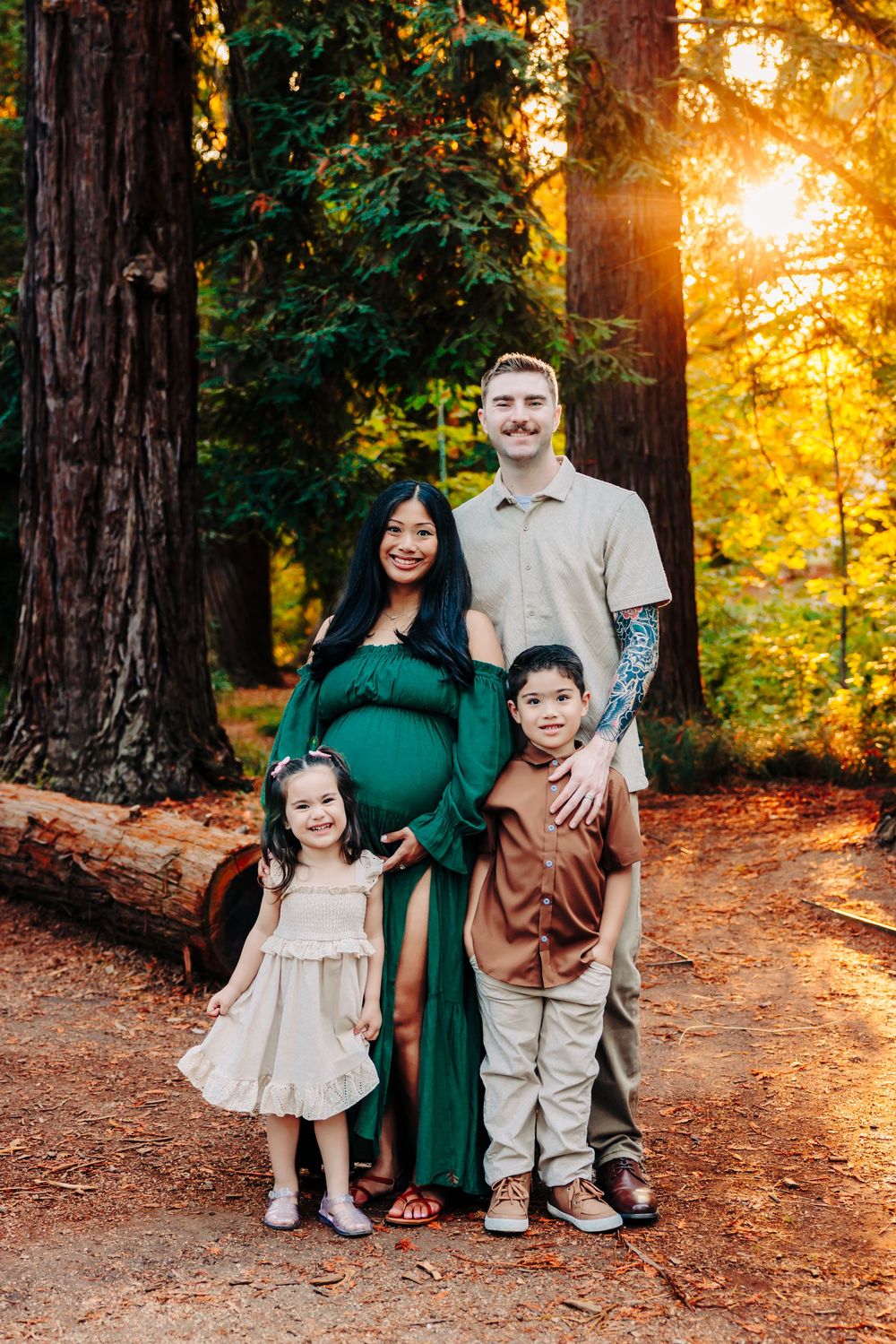 A family poses together in a redwood forest at sunset with golden light filtering through the trees.