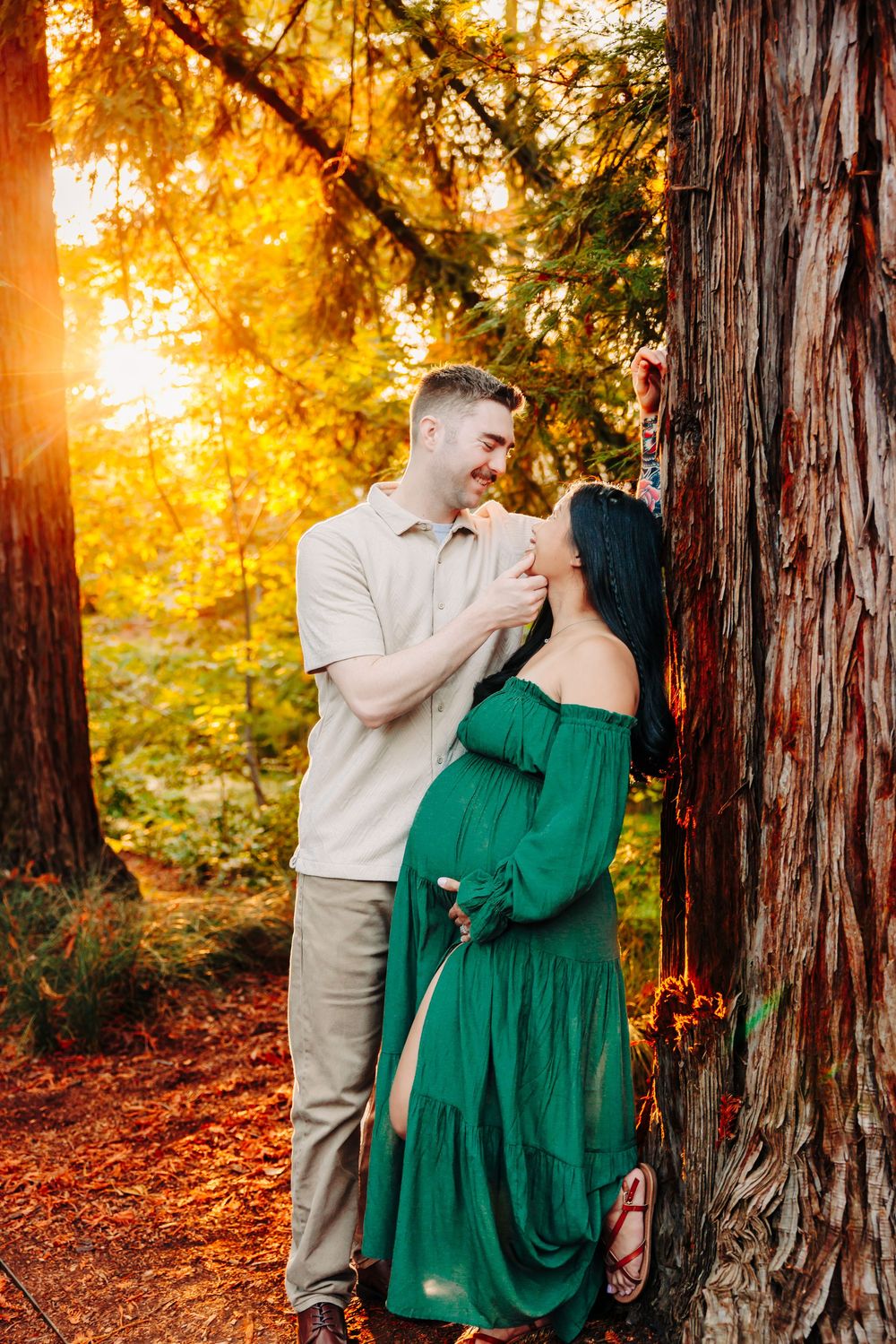 Couple sharing intimate moments among towering redwood trees during golden hour.