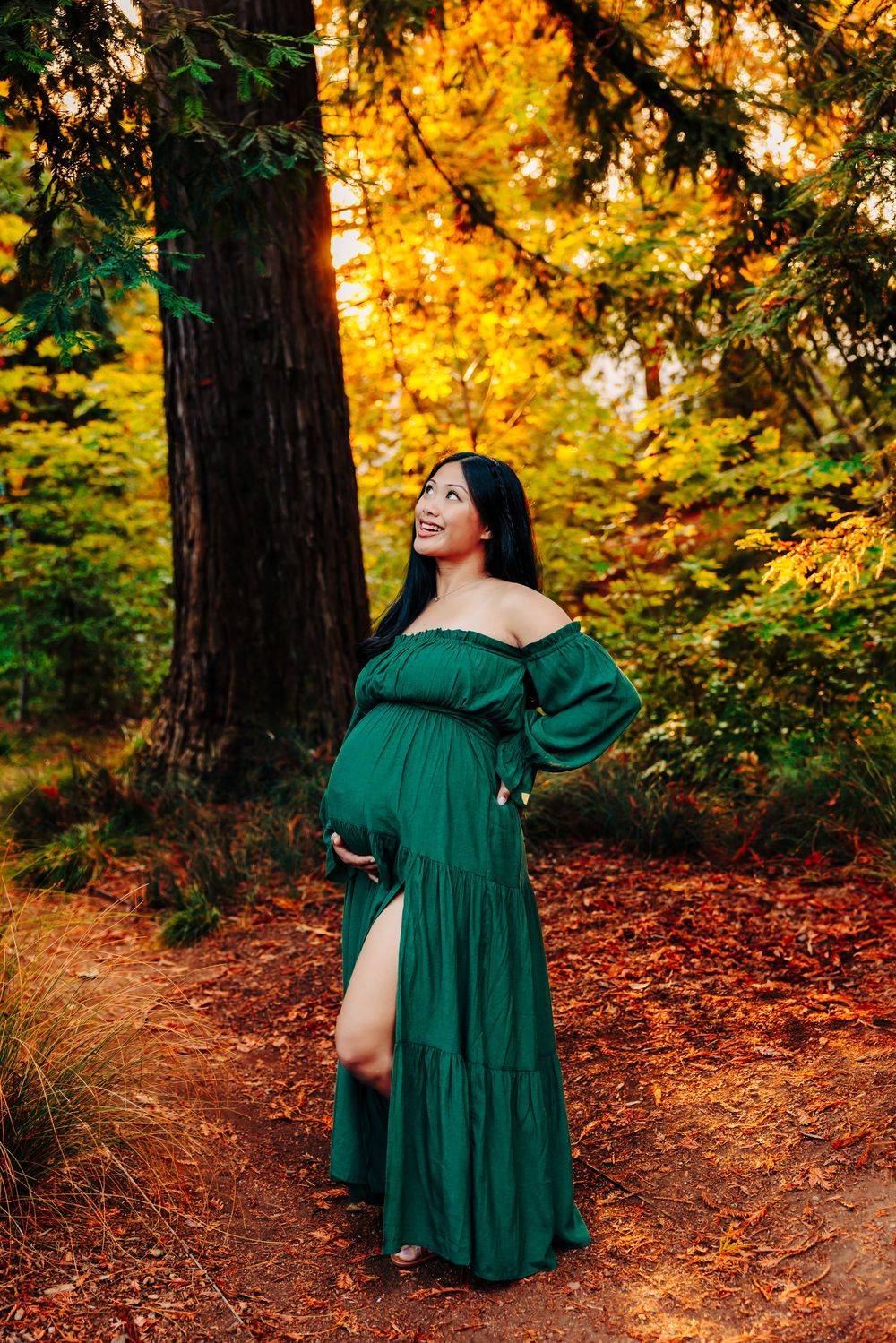 Emerald green dress flows gracefully against autumn foliage in wooded setting during sunset.