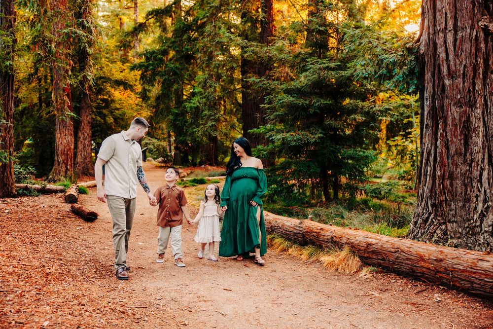A family walks together on a fallen log path through a forest with vibrant autumn foliage in the background.