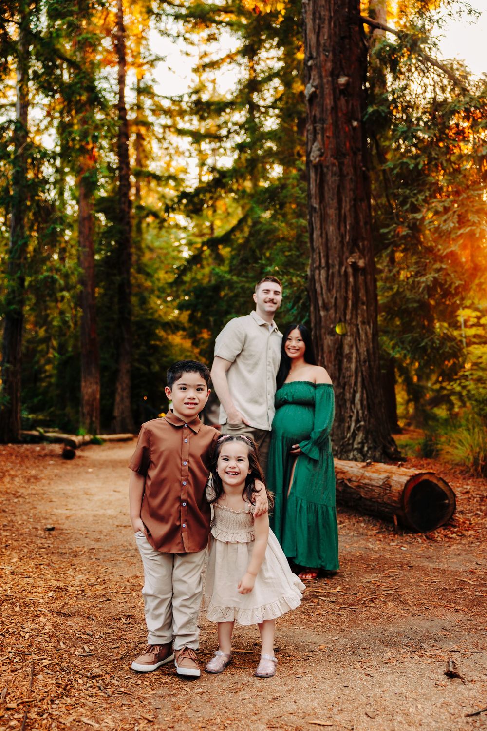 Family portrait session in autumn forest with fallen leaves and tall trees during golden hour.
