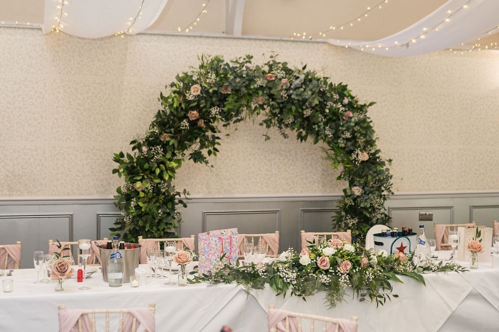 Wedding reception room with greenery arch and fairy lights on ceiling.