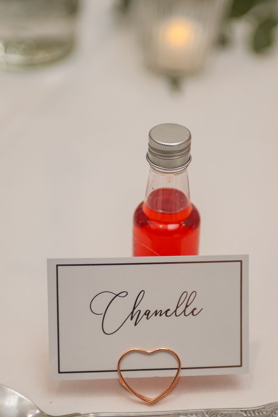 Small red drink bottles with name cards and heart decorations on white tablecloth.