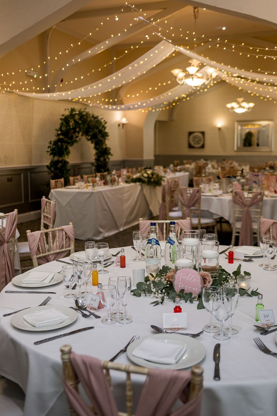 Wedding reception tables set with white linens and pink chair sashes.