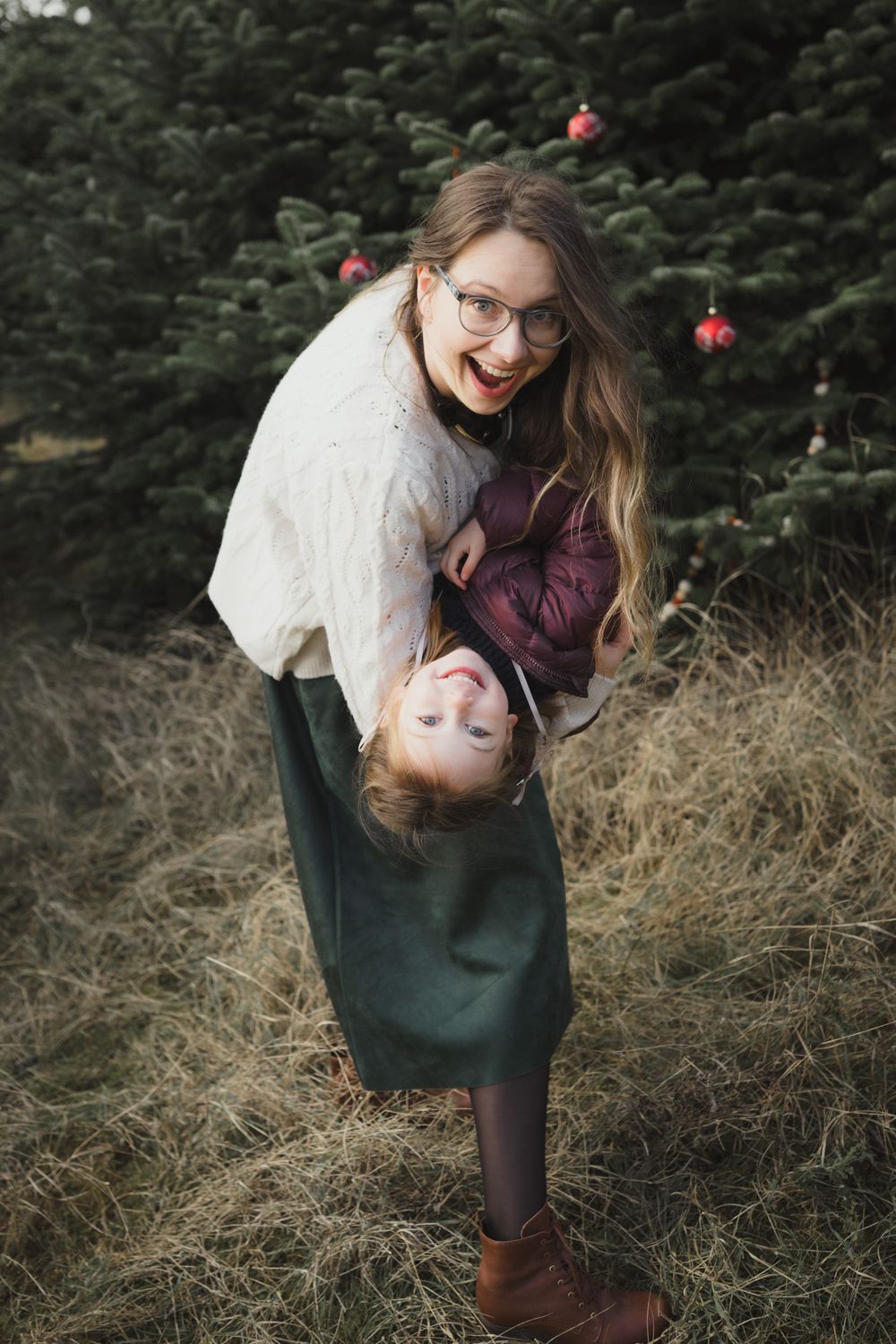 Playful couple sharing a romantic moment among evergreen trees during a winter photoshoot.