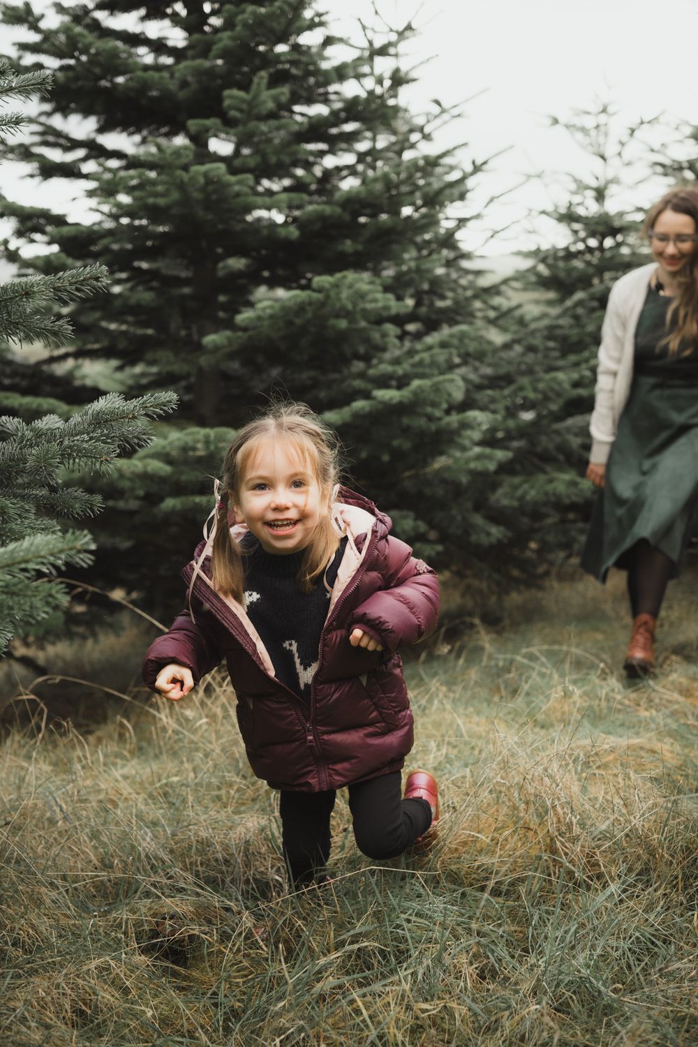 A sequence of photos showing a child in a burgundy winter coat crouching in tall grass near an evergreen tree.