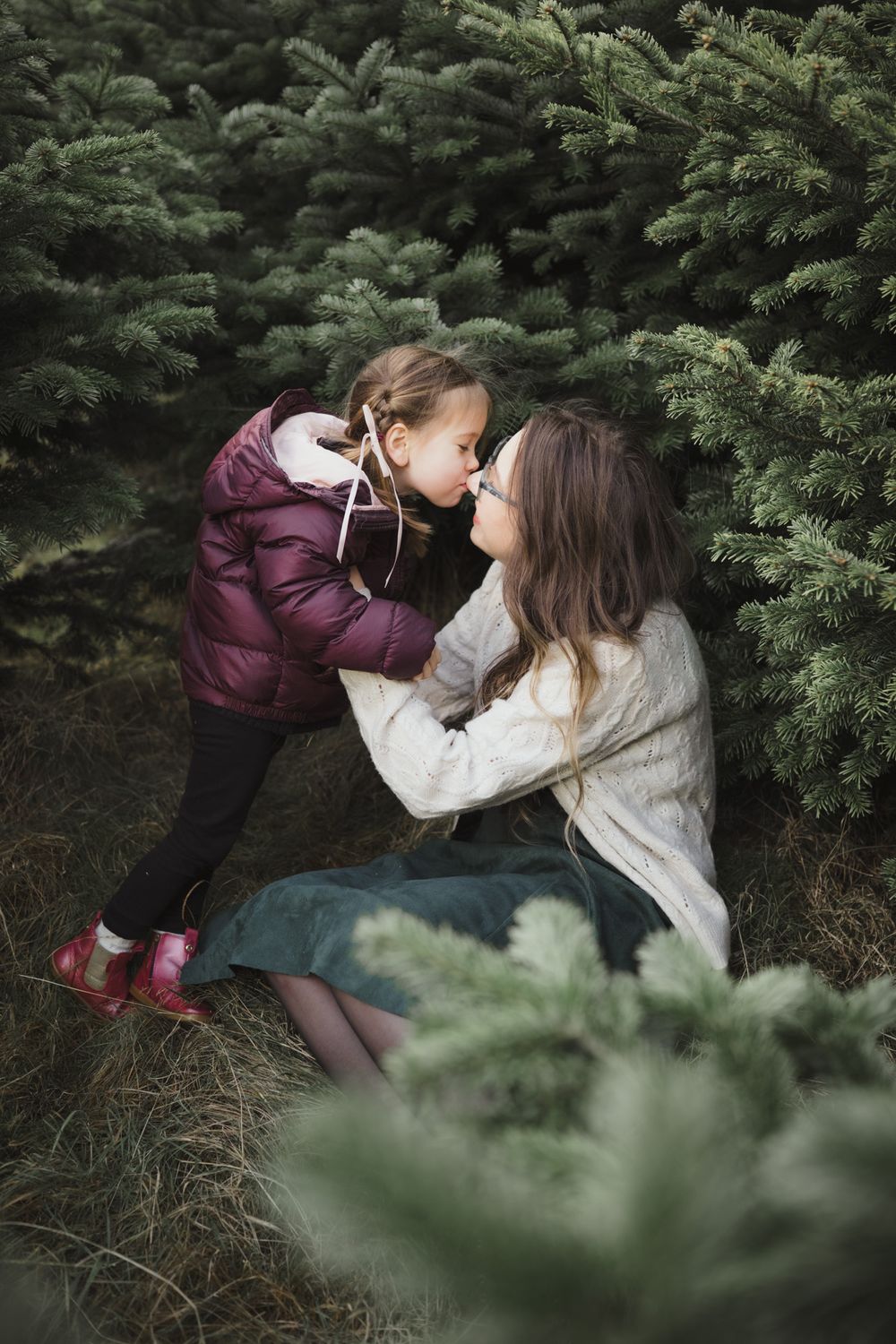 A touching moment between parent and child playing together in front of evergreen trees in a forest setting.