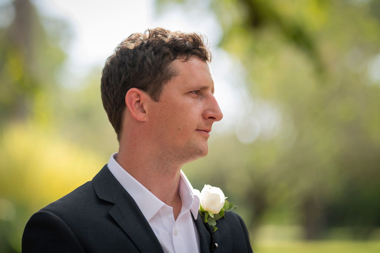 A series of profile shots showing a groom in a black suit with a white boutonniere in an outdoor garden setting.