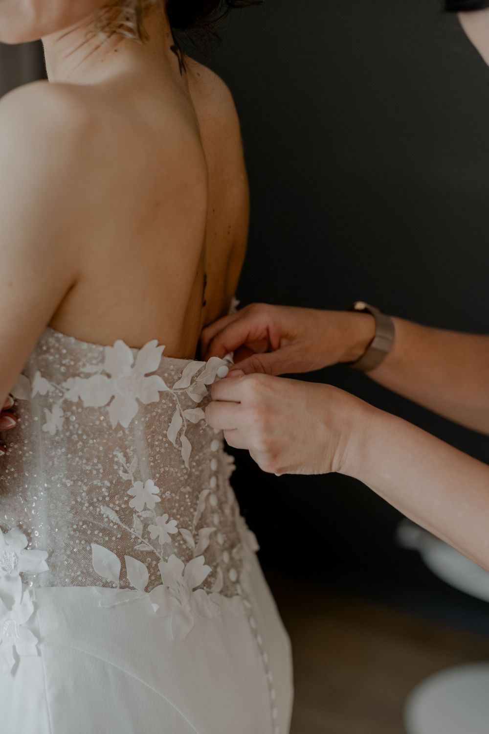 Im KPM Hotel beim Getting Ready hilft die Stylisten der Braut beim Anziehen ihres Brautkleid. Sie macht den Reisverschluss zu.