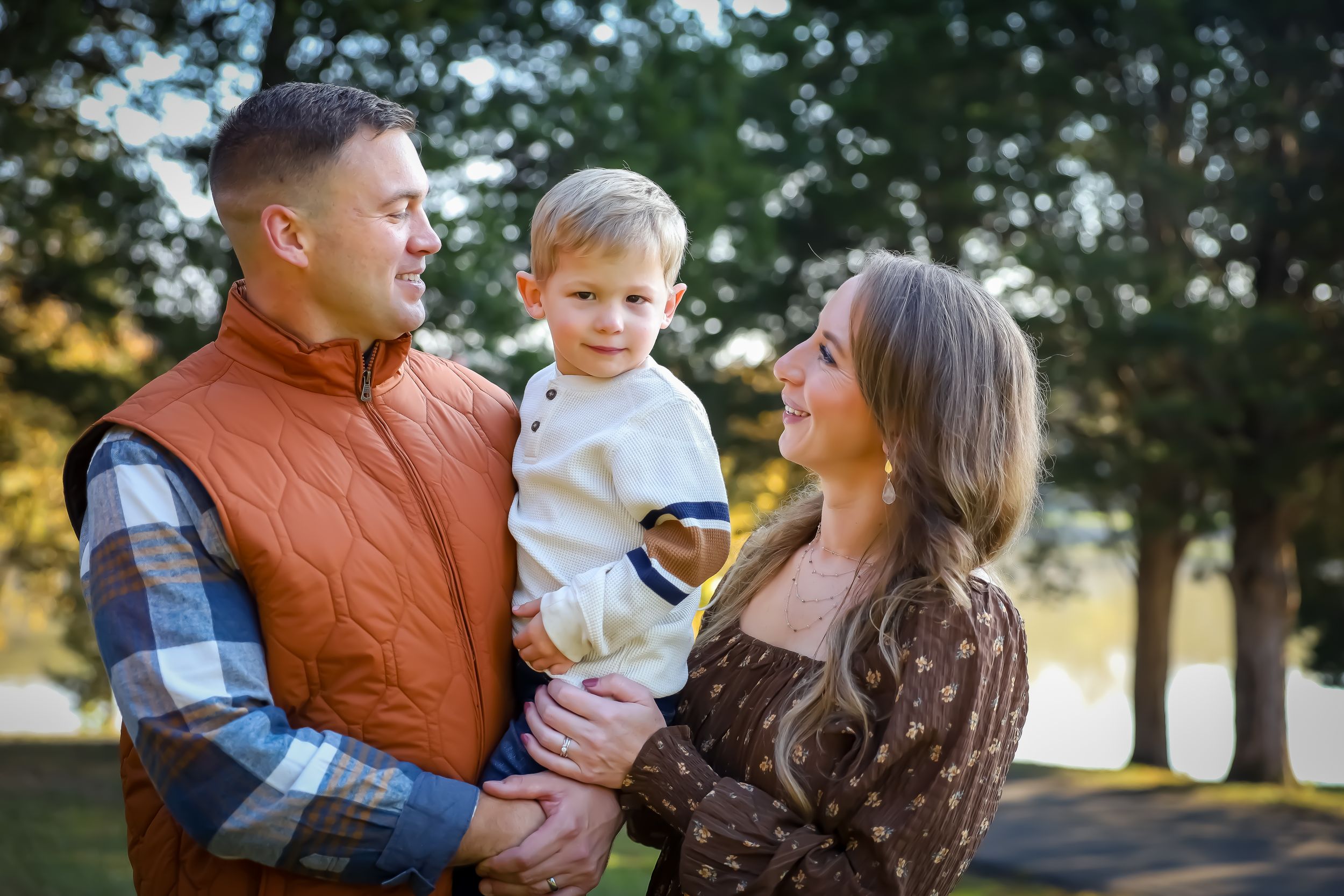 Family of three in autumn attire sharing a tender moment outdoors.