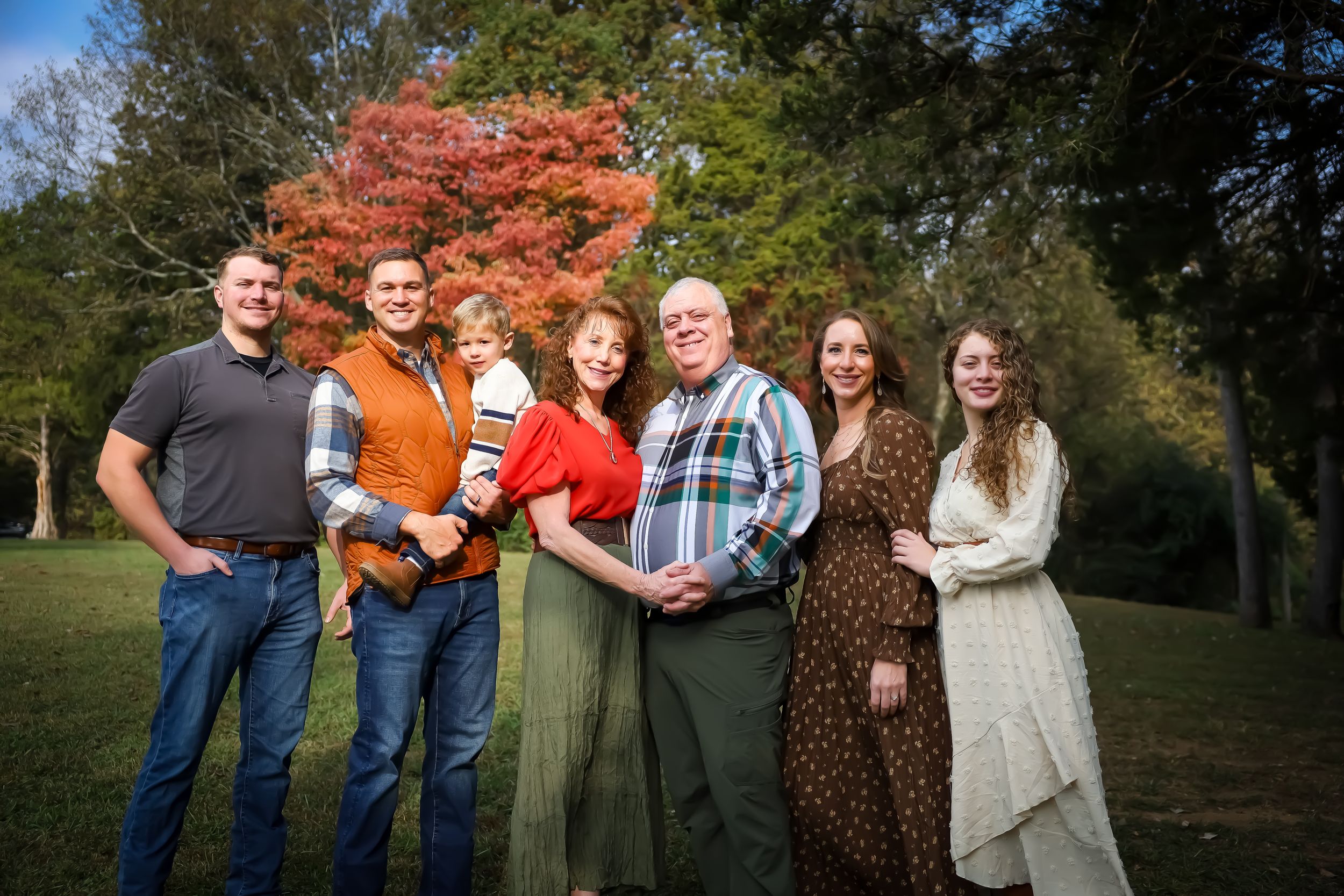 Extended family gathering outdoors with vibrant red maple tree in background.