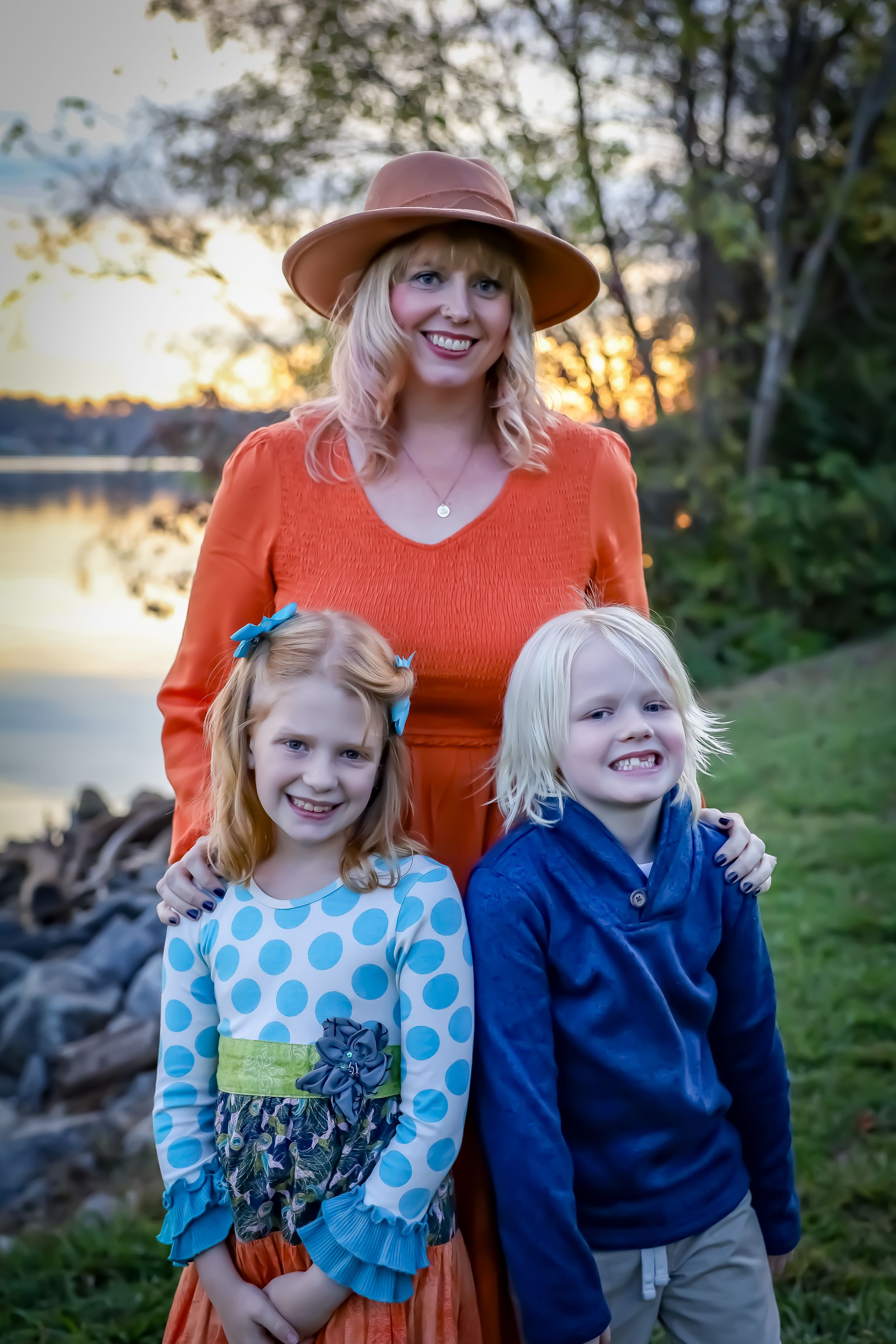 Family portrait at sunset by a lake with orange and blue outfits against an autumn backdrop.
